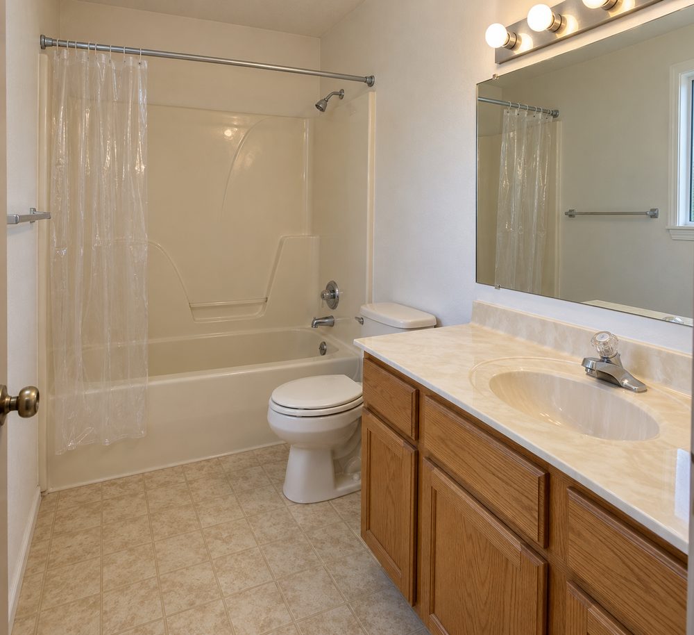Dated 1990s hall bathroom with an almond fiberglass tub surround, a curtain, an oak vanity and a cultured marble top